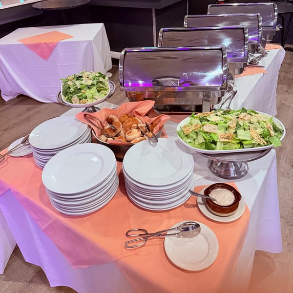A buffet table with Caesar salad, bread rolls, and chafing dishes, ready for serving.