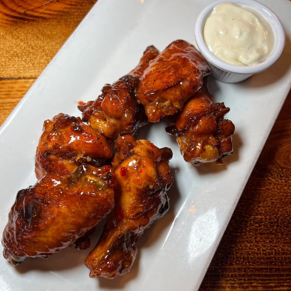 Glazed chicken wings with a side of creamy dipping sauce on a white rectangular plate.