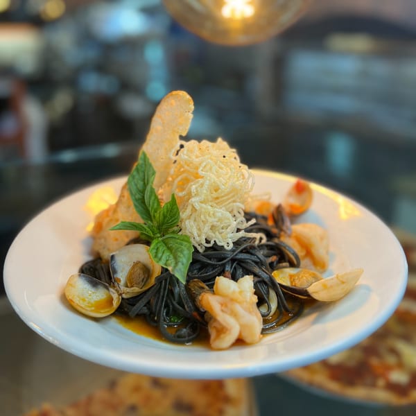 Black squid ink pasta with clams, shrimp, crispy noodles, and basil on a white plate.