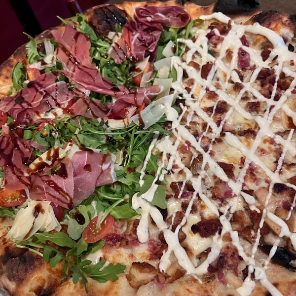 Half prosciutto and arugula pizza with balsamic glaze, half bacon and chicken pizza with white sauce.