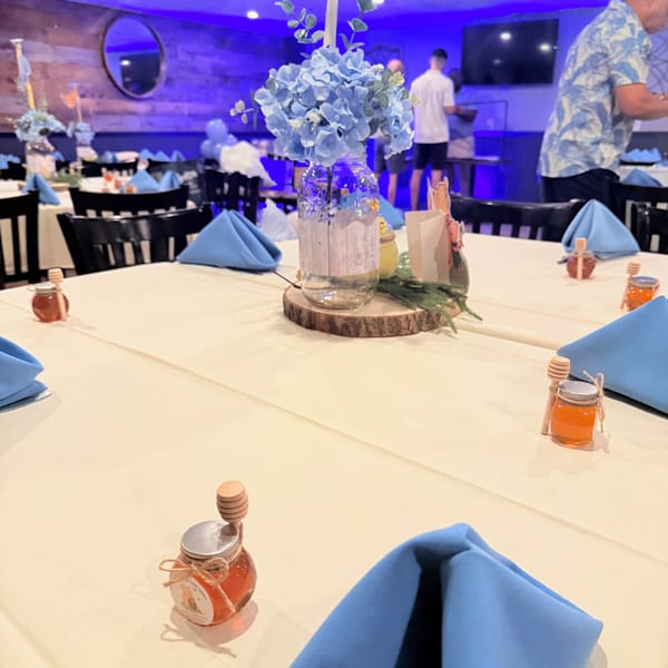 Tables set with blue napkins, honey jars, and floral centerpieces under blue lighting at Franco Martini Bar & Restaurant.