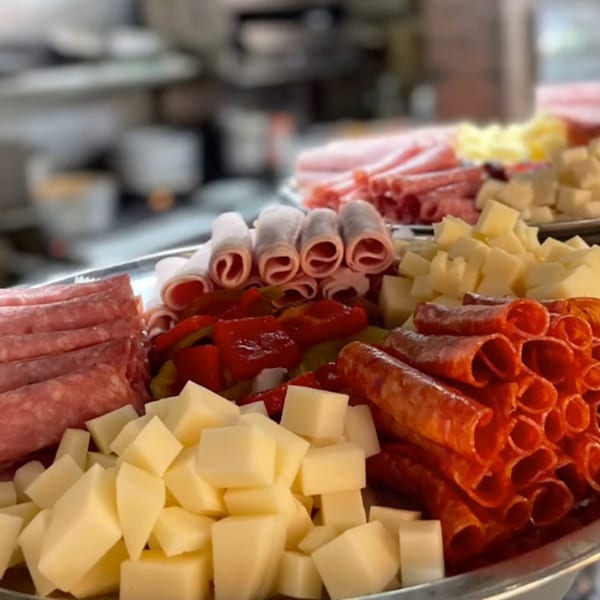 A platter of Italian antipasto with rolled meats, cubed cheeses, and roasted red peppers.