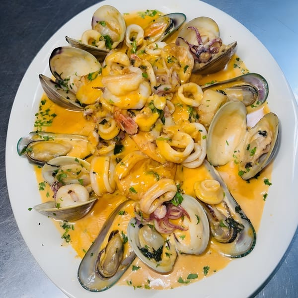 A white plate filled with Italian seafood, including clams, mussels, and calamari in a rich orange sauce.