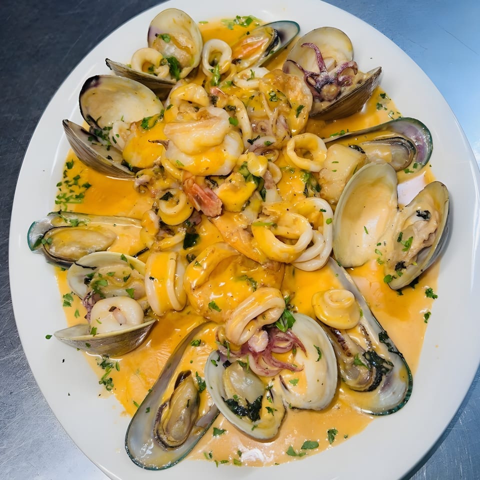 A white plate filled with Italian seafood, including clams, mussels, and calamari in a rich orange sauce.
