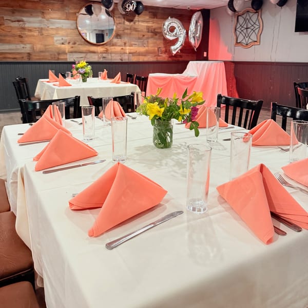 Tables set with white tablecloths, coral napkins, and floral centerpieces, with "90" balloons in the background.