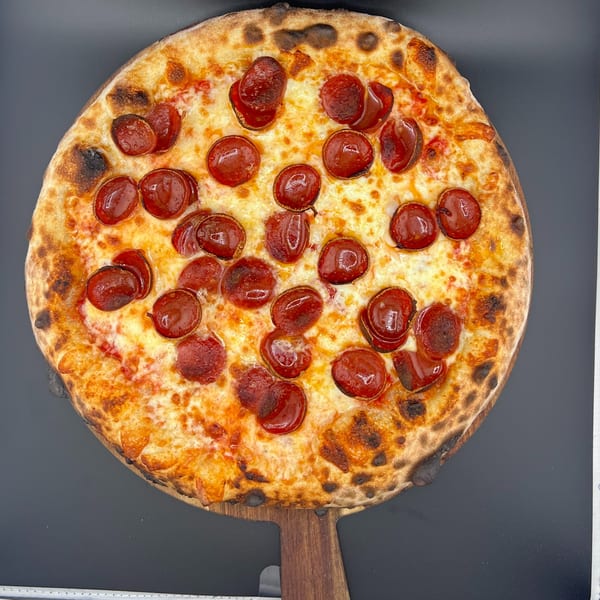 A whole pepperoni pizza with a golden-brown crust and melted cheese on a wooden pizza peel.