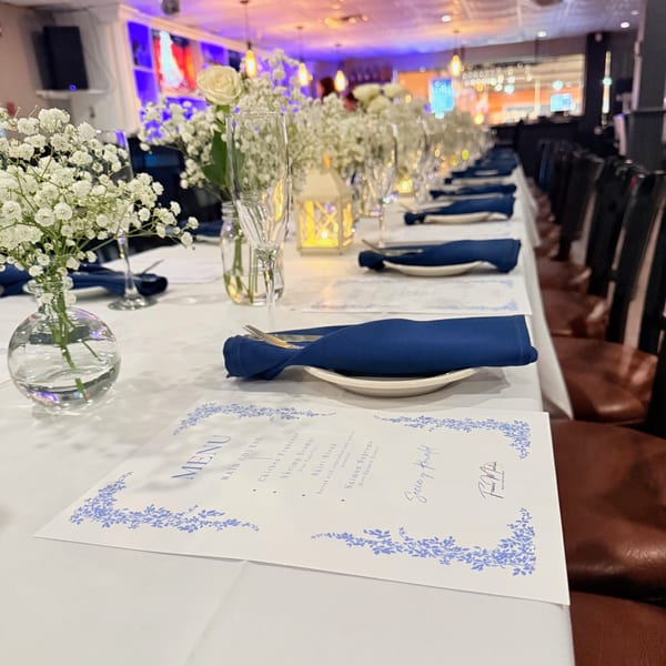 A long dining table set with white tablecloths, blue napkins, menus, and floral centerpieces at Franco Martini.