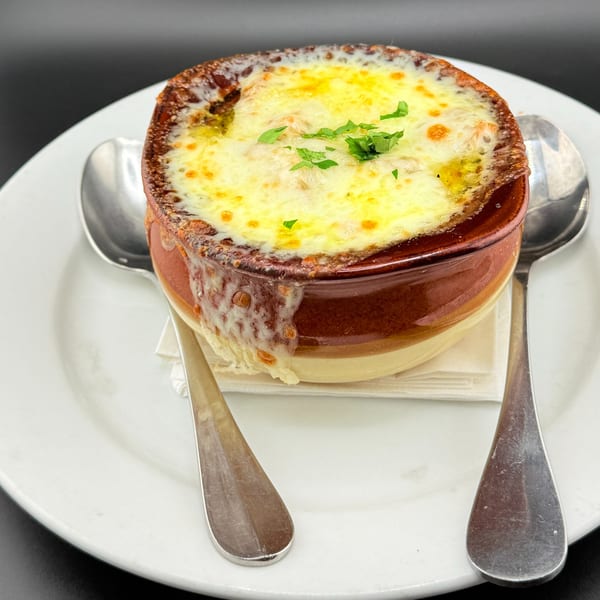 A crock of Franco Martini's Italian onion soup with melted cheese and parsley, served with spoons.