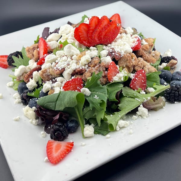 A vibrant salad with mixed greens, strawberries, blueberries, blackberries, candied pecans, and crumbled feta cheese.